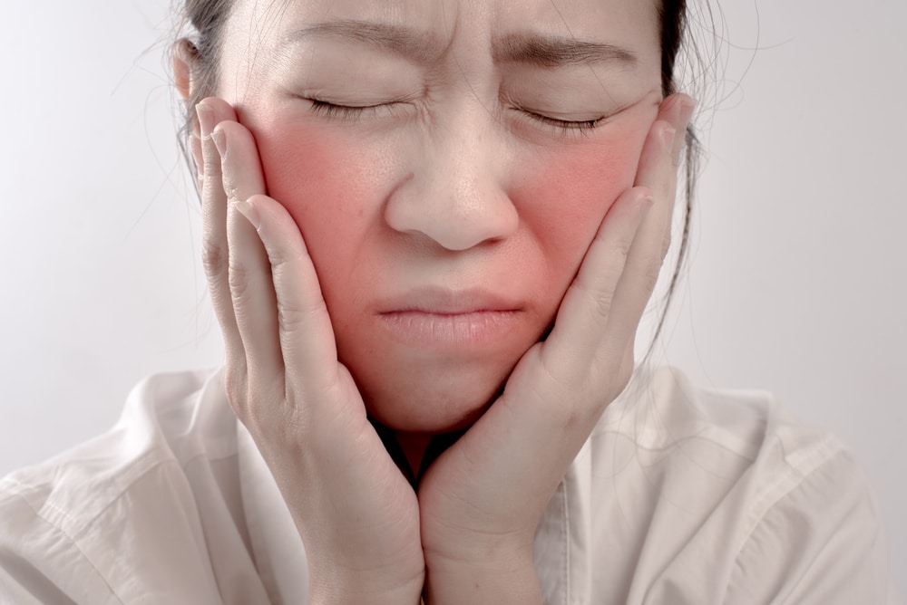Asian woman with irritated facial skin holds her face.